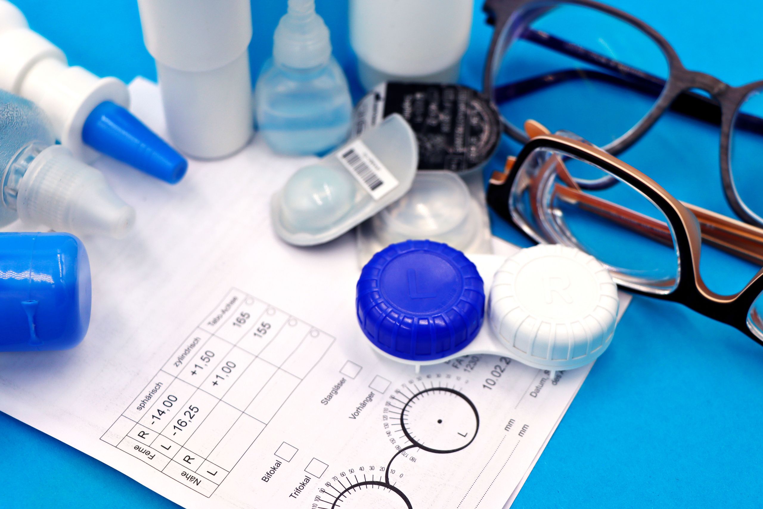 Close-up of contact lenses, case, and eyeglasses on a prescription form.